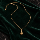 Collar Gota Dorada delicado sobre terciopelo verde oscuro y mármol negro.