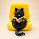 Figura decorativa de gato negro lector en sillón amarillo