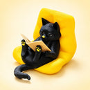 Figura decorativa de gato negro lector en sillón amarillo